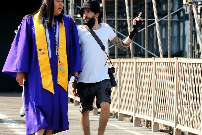 two people leaving an NYU graduation cross the Brooklyn Bridge